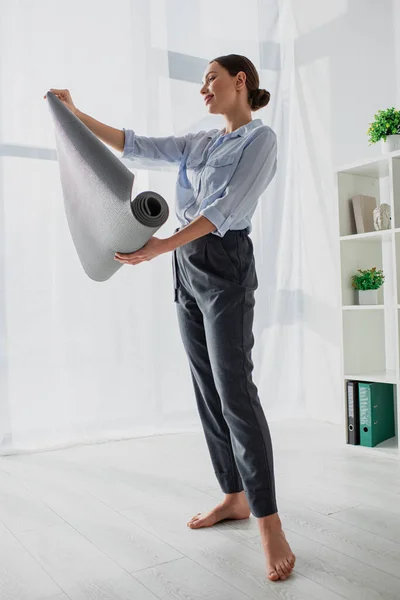 Belle jeune femme d'affaires souriante tenant tapis de yoga dans le bureau — Photo de stock