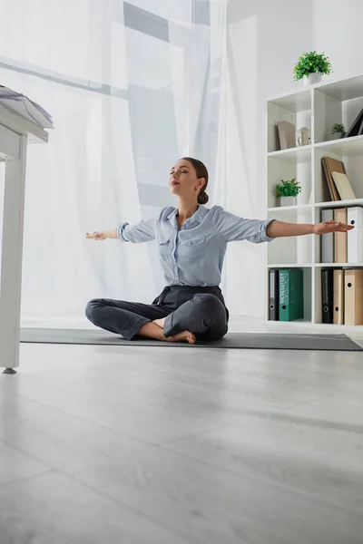 Young businesswoman practicing yoga in lotus position on mat in office — Stock Photo