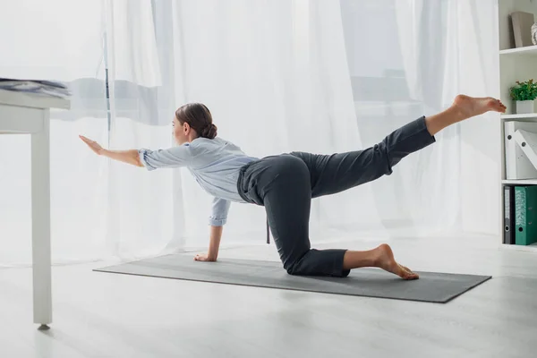 Businesswoman practicing yoga in bird dog pose on mat in office — Stock Photo
