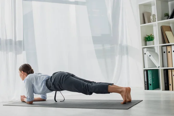 Beautiful businesswoman practicing yoga in plank on mat in office — Stock Photo