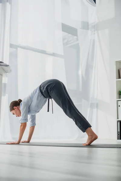 Empresaria practicando yoga en postura Downward-Facing Dog sobre alfombra en oficina — Stock Photo