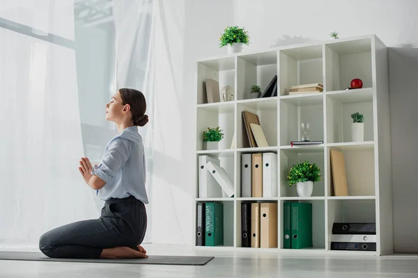 Businesswoman practicing yoga and meditating with namaste gesture on mat in office — Stock Photo