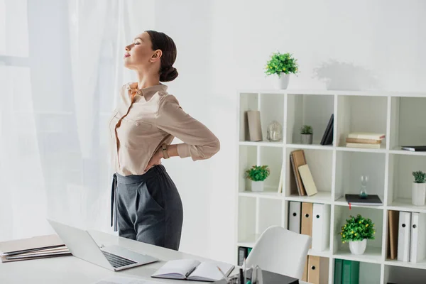 Tired businesswoman stretching back at workplace in modern office — Stock Photo
