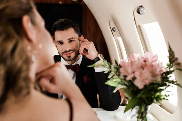 Selektiver Fokus der Frau am Tisch gegenüber lächelndem, elegantem Mann im Flugzeug — Stockfoto