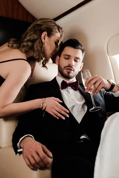 Femme sensuelle touchant homme élégant tenant verre de champagne dans l'avion — Photo de stock