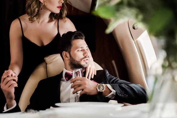Обрезанный вид сексуальной женщины, касающейся элегантного мужчины, держащего бокал шампанского в самолете — стоковое фото
