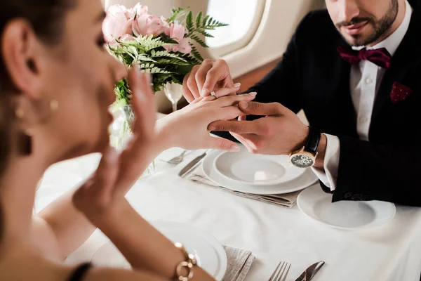 Selective focus of man putting wedding ring on finger on surprised woman while making marriage proposal in plane — Stock Photo