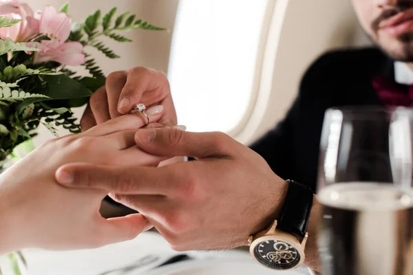 Vista cortada do homem colocando anel de casamento no dedo sobre a mulher ao fazer proposta de casamento no avião — Fotografia de Stock