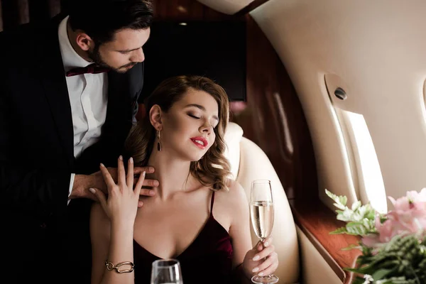 Elegante hombre tocando sexy mujer sosteniendo copa de champán en avión - foto de stock