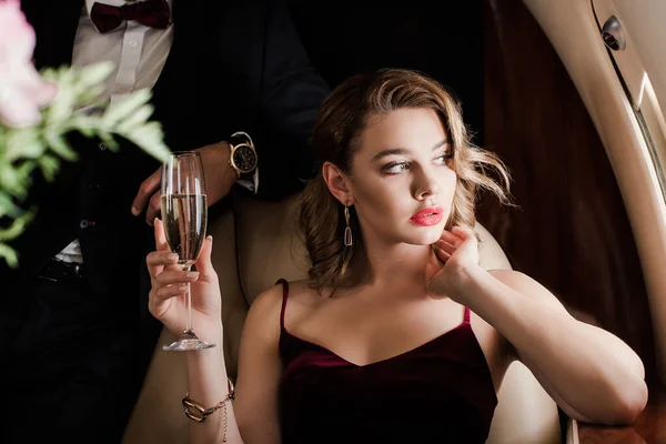 Cropped view of man standing near pensive, beautiful woman holding glass of champagne in plane — Stock Photo