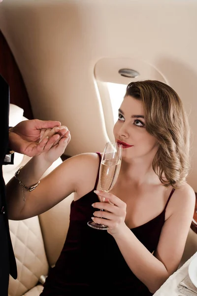 Обрізаний вид чоловіка тримає руку привабливої усміхненої жінки з келихом шампанського — стокове фото