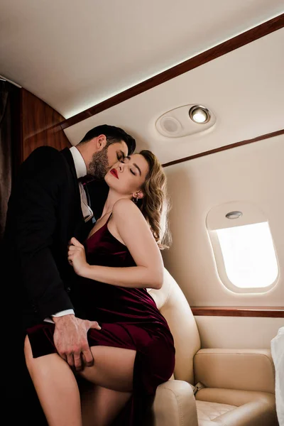 Homem elegante tocando perna e beijando mulher apaixonada no avião — Fotografia de Stock