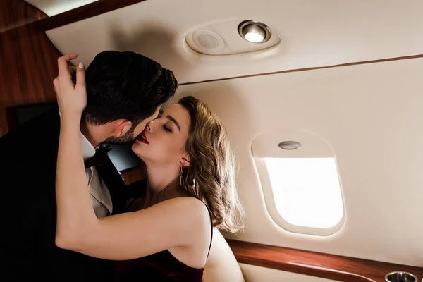 Elegante, jovem casal abraçando e beijando no avião — Fotografia de Stock