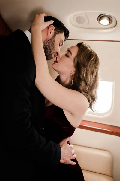 Schöner Mann umarmt und küsst sexy, elegante Frau im Flugzeug — Stockfoto