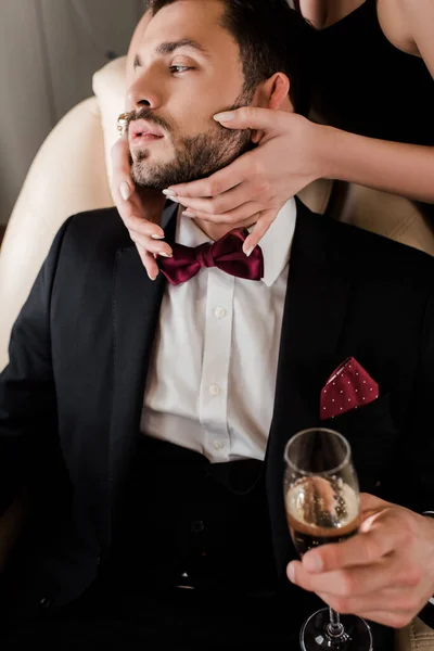 Abgeschnittene Ansicht einer Frau, die das Gesicht eines gutaussehenden Mannes berührt, der ein Glas Champagner hält — Stockfoto