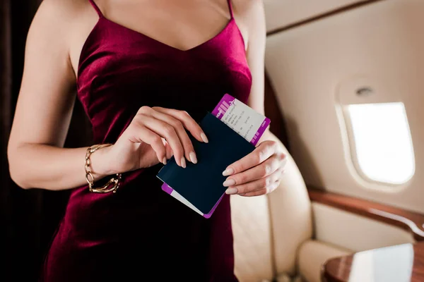 Cropped view of sexy woman in elegant dress holding passport and air ticket — Stock Photo