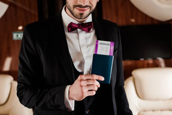 Cropped view of elegant man holding passport and air ticket in plane — Stock Photo