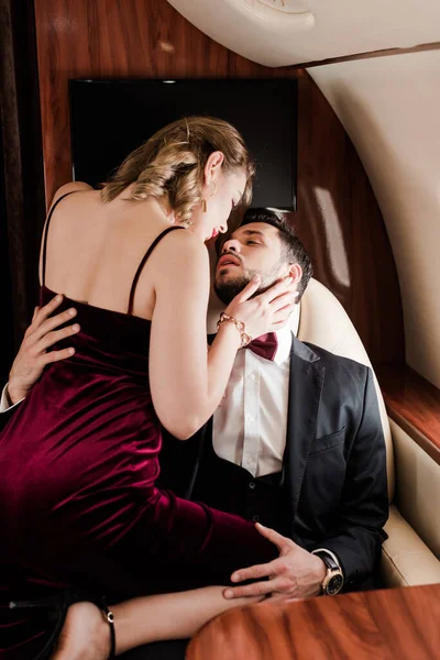 Handsome man embracing sexy, elegant woman sitting on his laps in plane — Stock Photo