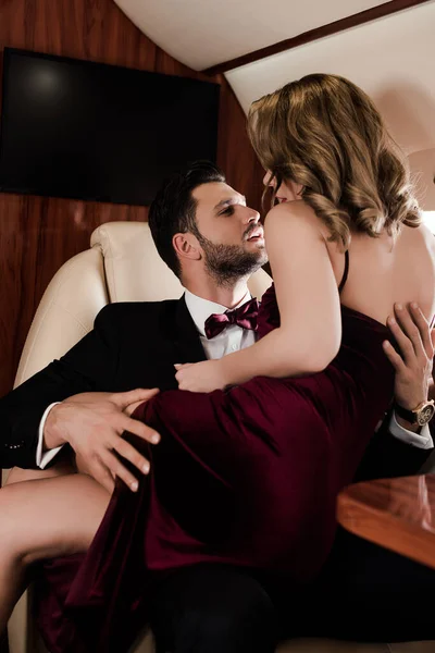 Елегантний чоловік обіймає чуттєву жінку, сидячи на колінах у літаку — стокове фото