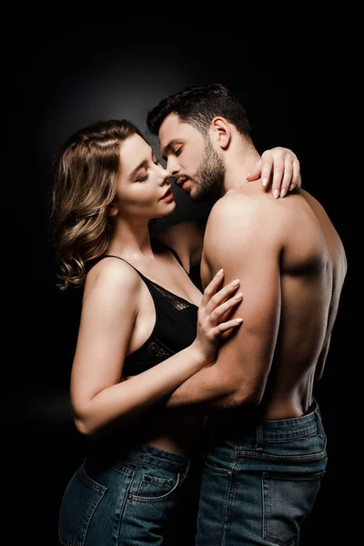 Sexy shirtless man and passionated girl in blue jeans embracing on black background — Stock Photo