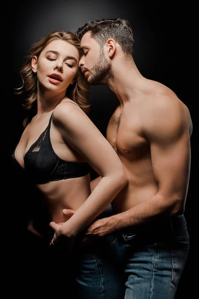 Shirtless, muscular man hugging attractive girlfriend in bra isolated on black — Stock Photo