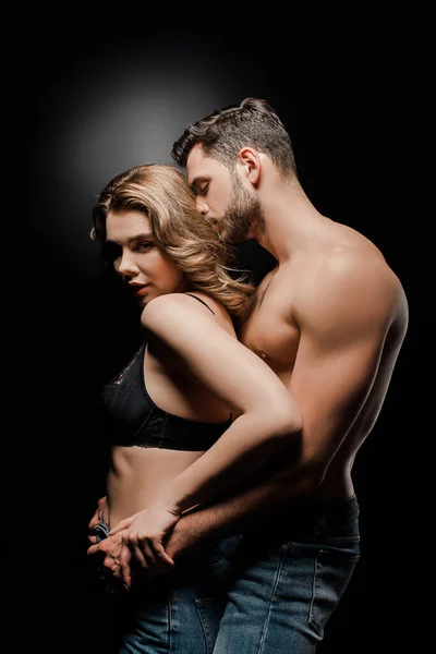 Sexy muscular man embracing and kissing attractive girl in bra on black background — Stock Photo