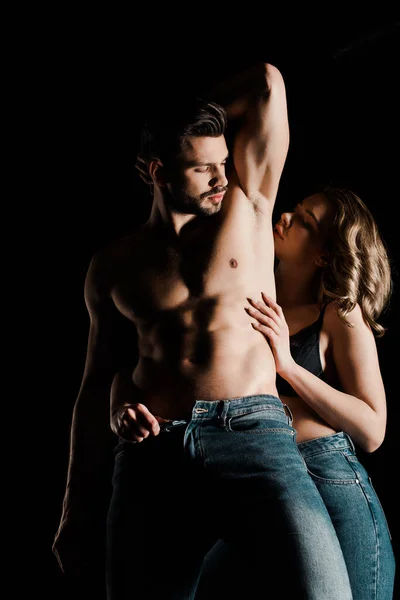 Seductive girl unbuttoning jeans of sexy boyfriend isolated on black — Stock Photo