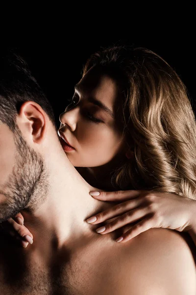Сексуальна молода жінка обіймає чоловіка і цілує його шию ізольовану на чорному — стокове фото