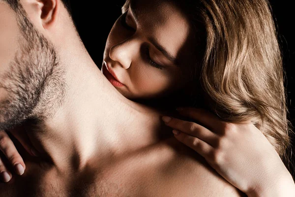 Sensuale giovane donna abbracciare l'uomo e baciare il collo isolato su nero — Foto stock