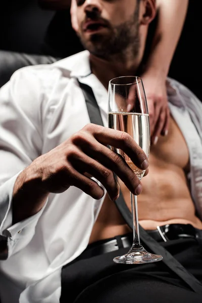 Обрезанный вид женщины касаясь сексуальный мужчина держа бокал шампанского изолирован на черном — стоковое фото