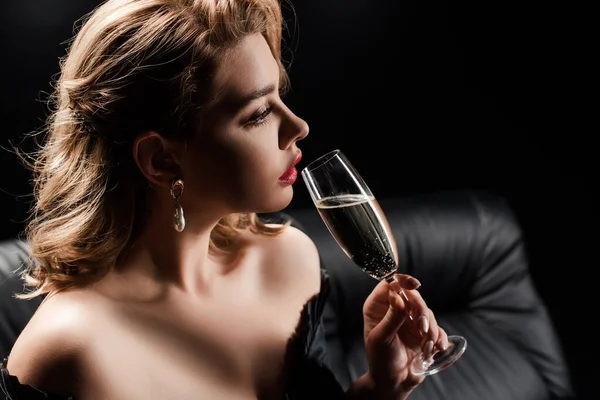 Elegante, nachdenkliche Frau hält ein Glas Champagner in der Hand, während sie isoliert auf schwarz wegschaut — Stockfoto