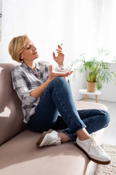 Happy and mature woman holding joint with medical cannabis and ashtray — Stock Photo