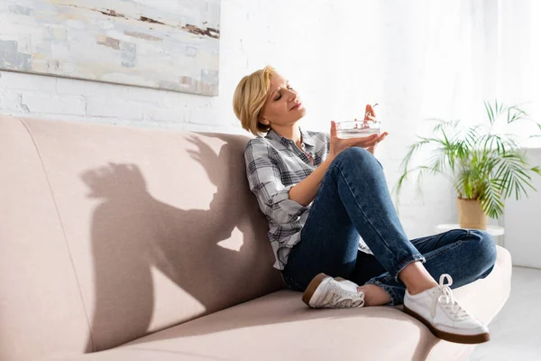 Cheerful and mature woman holding joint with medical cannabis and ashtray — Stock Photo