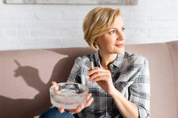 Messa a fuoco selettiva di donna felice e matura che tiene congiunta e posacenere — Foto stock