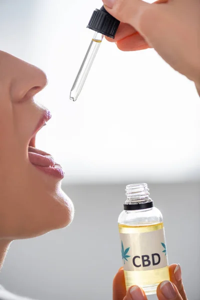 Vue recadrée de femme mature avec bouche ouverte tenant pipette et bouteille avec lettrage cbd — Photo de stock