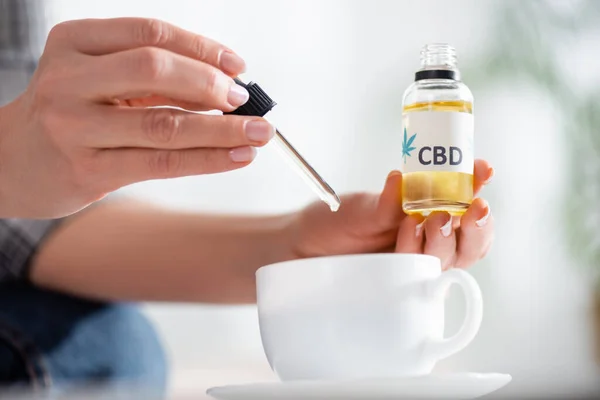 Vue recadrée de femme mature ajoutant une goutte de cbd dans une tasse de thé sur la table — Photo de stock