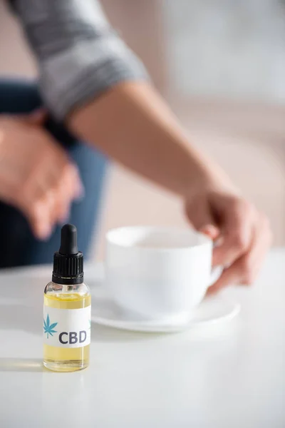 Selektiver Fokus der Flasche mit cbd-Schriftzug in der Nähe einer reifen Frau, die eine Tasse Tee berührt — Stockfoto