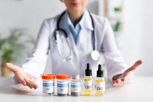 Cropped view of doctor pointing with hands at bottles with cbd and medical cannabis lettering — Stock Photo