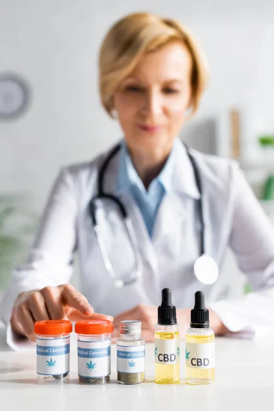 Enfoque selectivo del médico señalando con el dedo a la botella con letras de cannabis medicinal - foto de stock