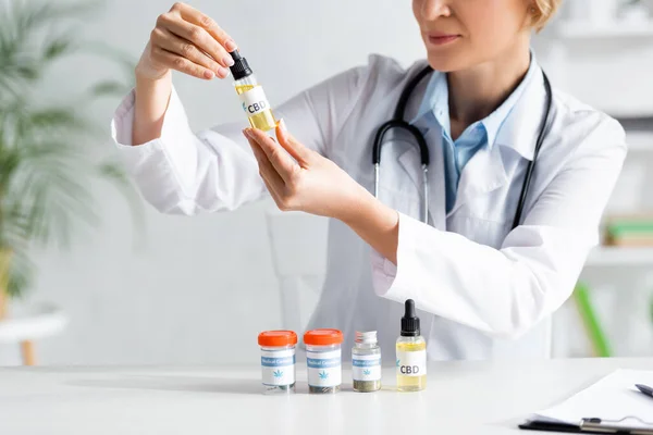 Vue recadrée du médecin en manteau blanc tenant bouteille avec lettrage cbd — Photo de stock