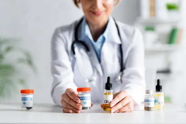 Vista cortada do médico em frascos de retenção de casaco branco com cbd e letras de cannabis medicinal — Fotografia de Stock