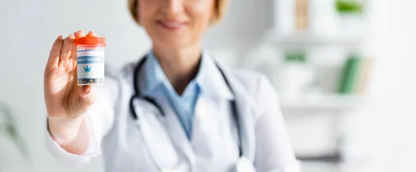 Panoramic shot of happy and mature doctor in white coat holding bottle with medical cannabis lettering — Stock Photo