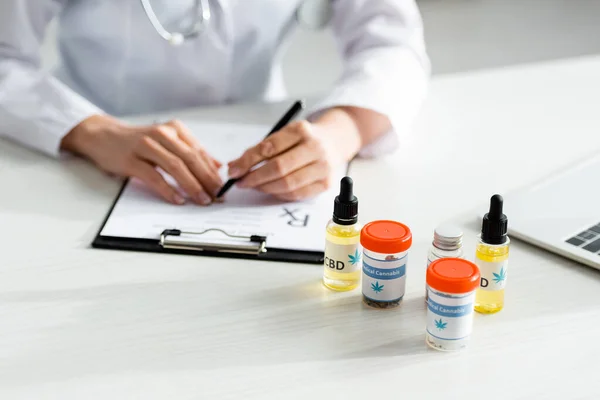 Selective focus of bottles with medical cannabis and cbd near doctor writing prescription — Stock Photo