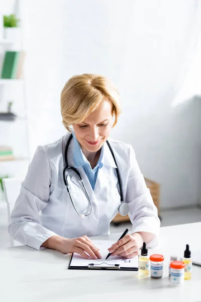 Selective focus of mature doctor writing prescription near bottles with medical cannabis and cbd lettering — Stock Photo