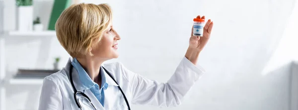 Panoramic shot of cheerful and mature doctor in white coat holding bottle with medical cannabis lettering — Stock Photo