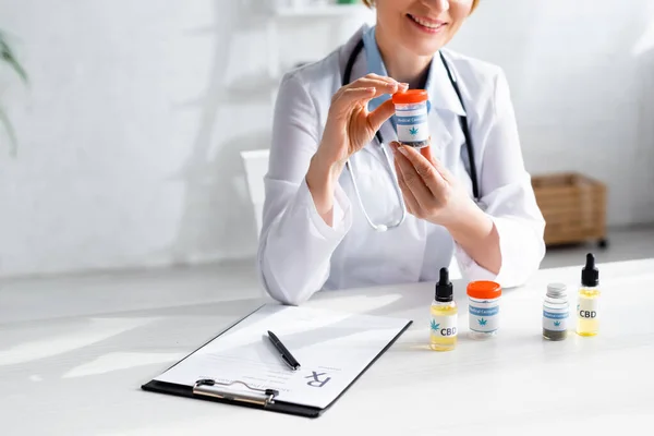 Vista cortada de médico feliz e maduro em garrafa de retenção casaco branco com letras cannabis medicinal — Fotografia de Stock
