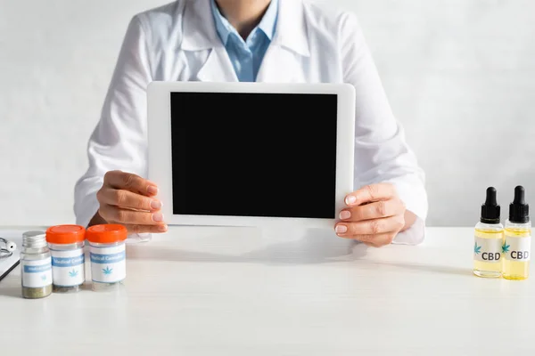 Cropped view of doctor holding digital tablet with blank screen near bottles with cbd and medical cannabis lettering in clinic — Stock Photo