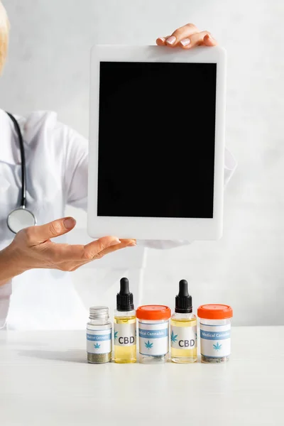 Cropped view of doctor holding digital tablet with blank screen near bottles with cbd and medical cannabis lettering in clinic — Stock Photo