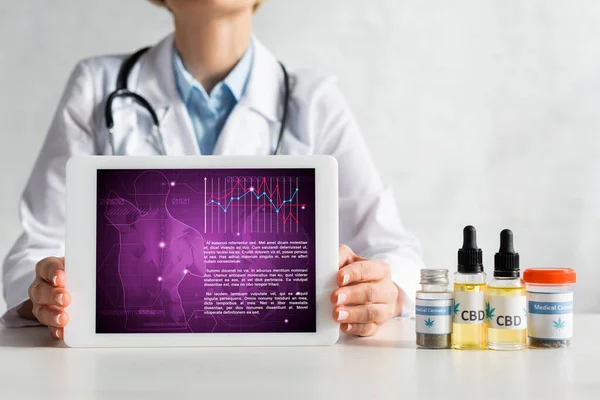 Vista ritagliata del medico maturo in possesso di tablet digitale con app medica vicino a bottiglie con scritte cbd — Foto stock