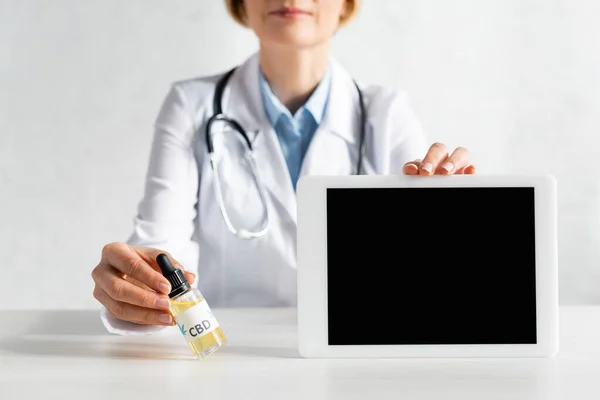 Cropped view of mature doctor in white coat holding digital tablet with blank screen and bottle with cbd lettering — Stock Photo